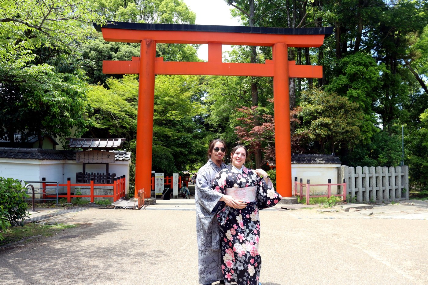 Pareja usando vestimenta tradicional y posando frente a un torii rojo.
