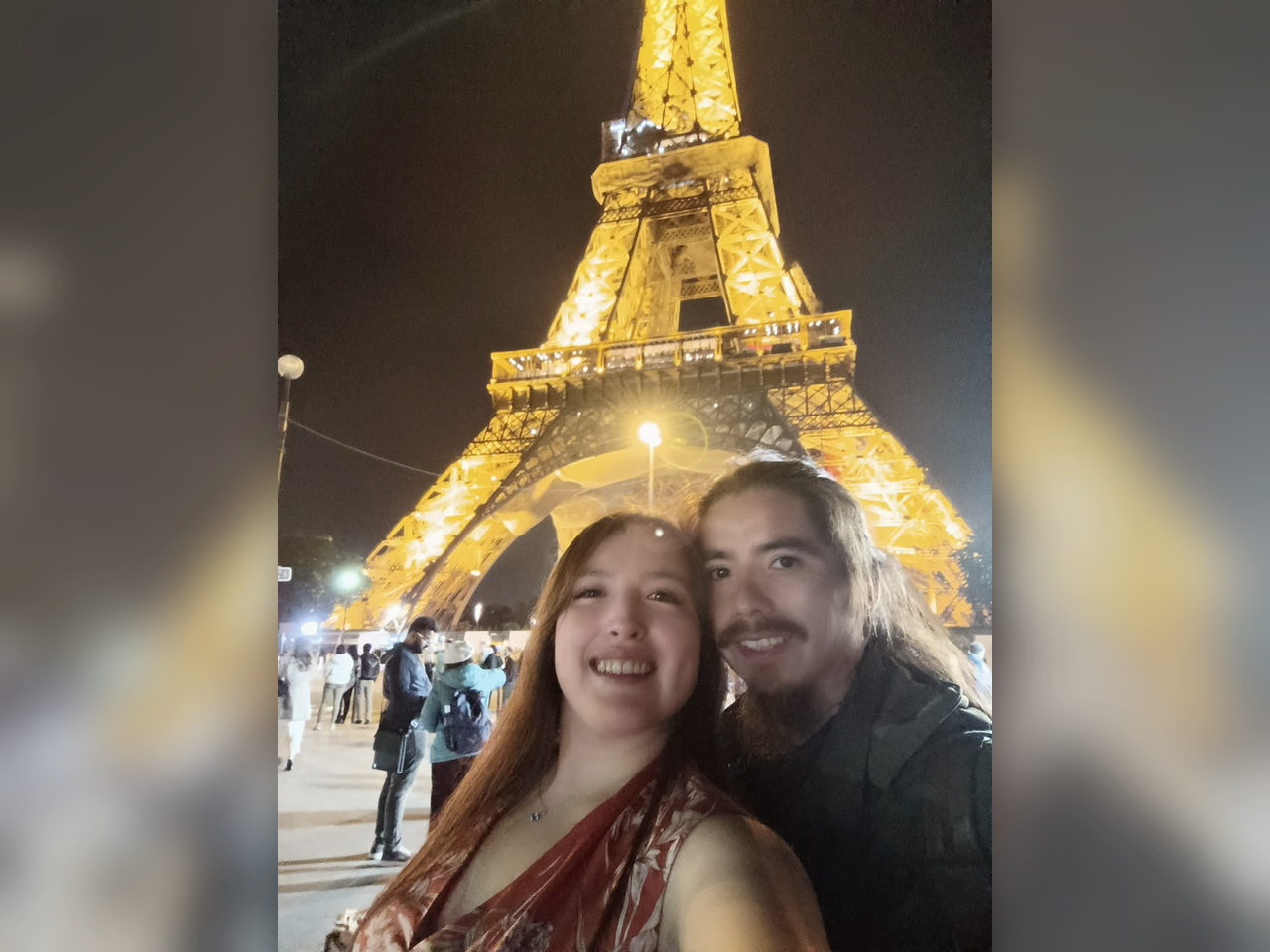 Selfie nocturna de la pareja frente a la Torre Eiffel iluminada.
