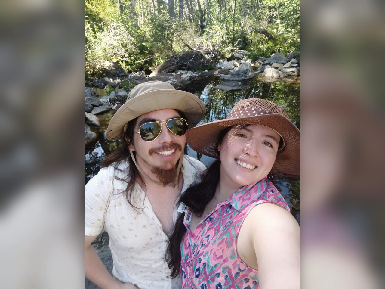 Selfie de la pareja usando sombreros junto a un río en la naturaleza.